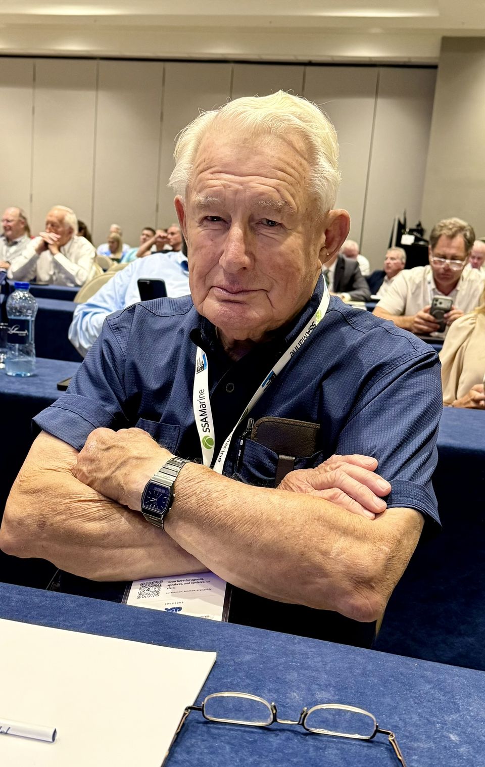 An attendee seated at a session table, arms crossed, smiling.