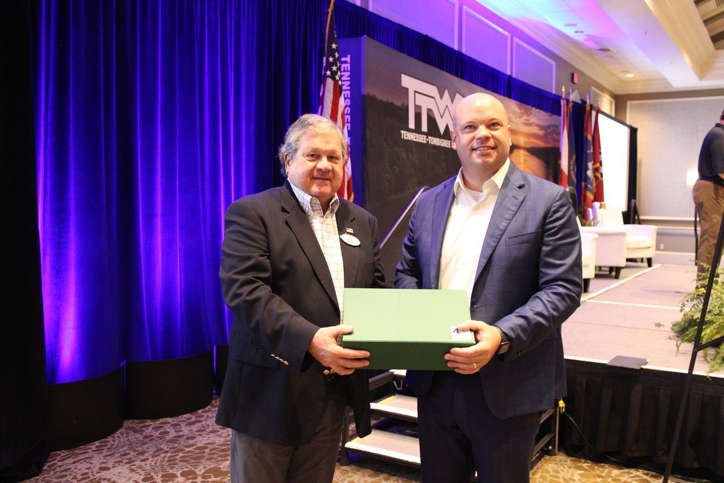 Two men hold a green gift box at the front of the ballroom.