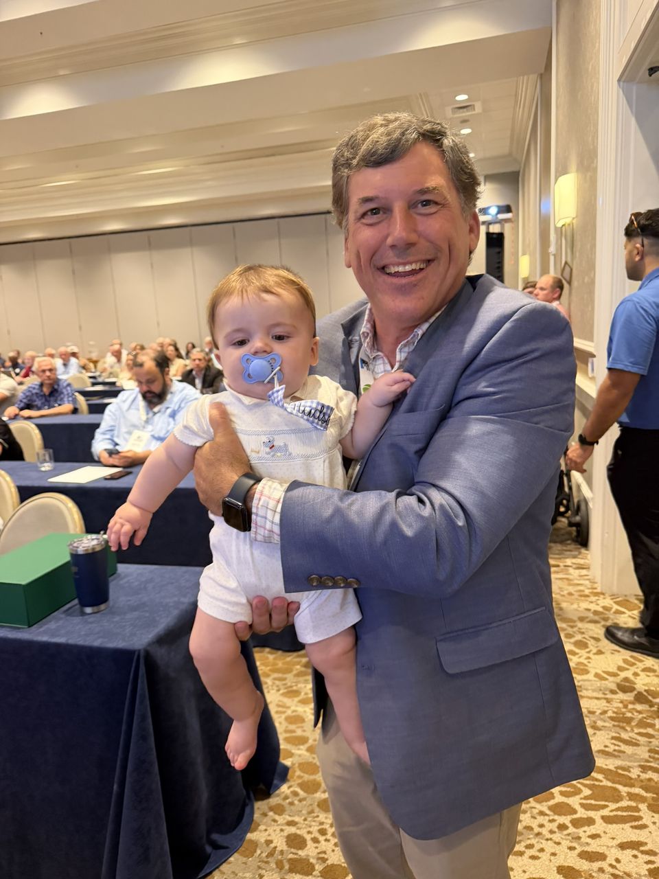 An attendee holds a baby in the ballroom.