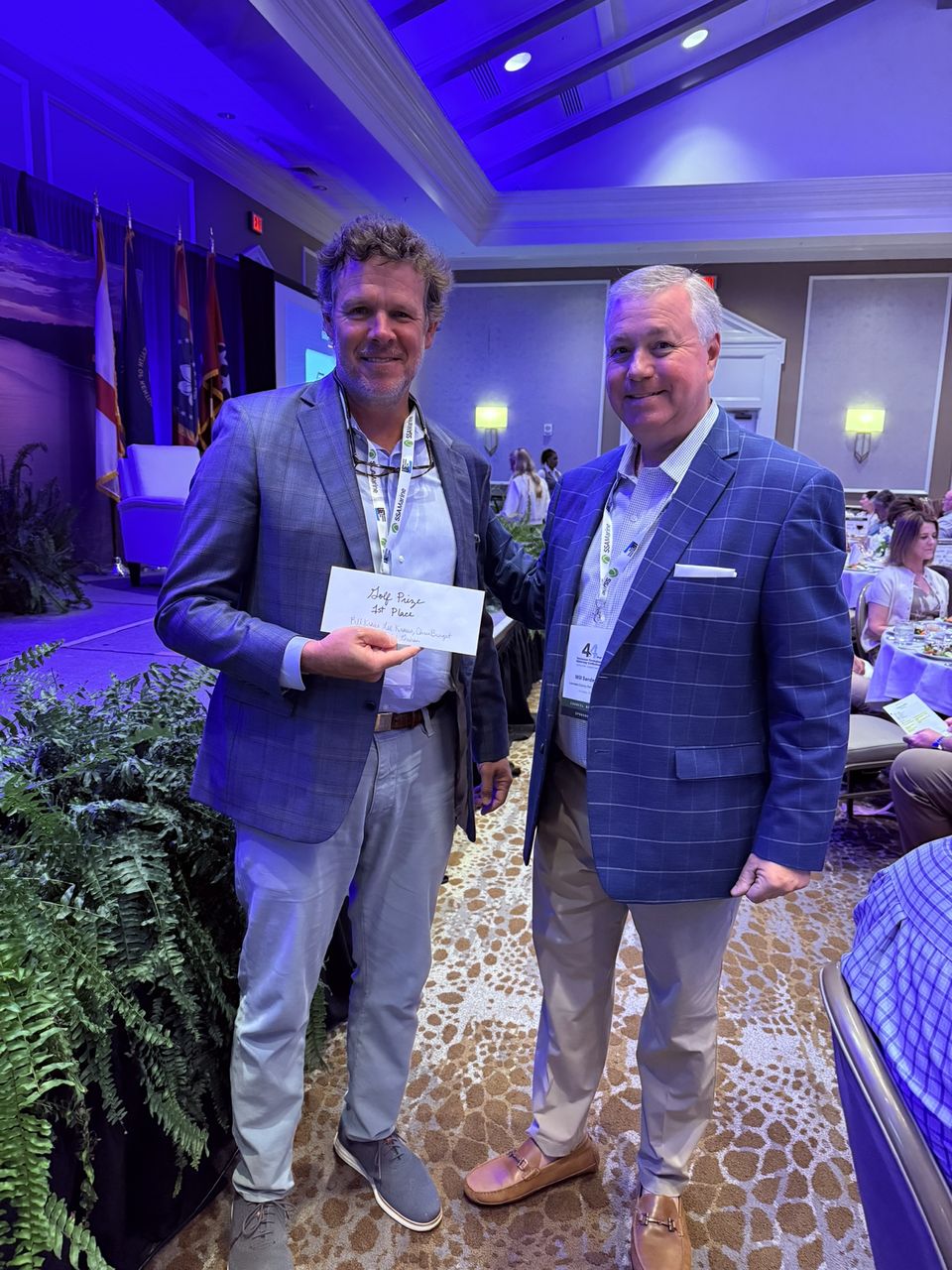 Two attendees pose, one holding an envelope.